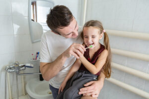 father helping his daughter brushing teeth