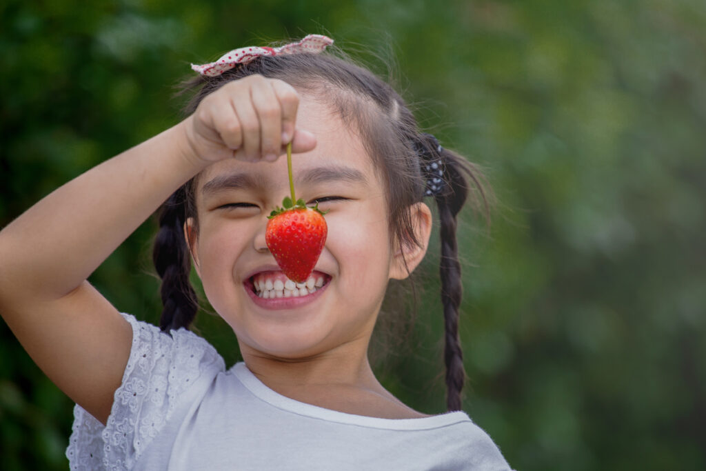 Beautiful little smiling girl eating strawberries in garden