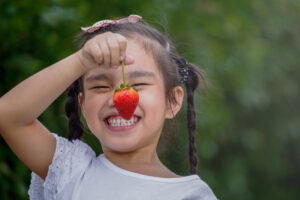 Beautiful little smiling girl eating strawberries in garden